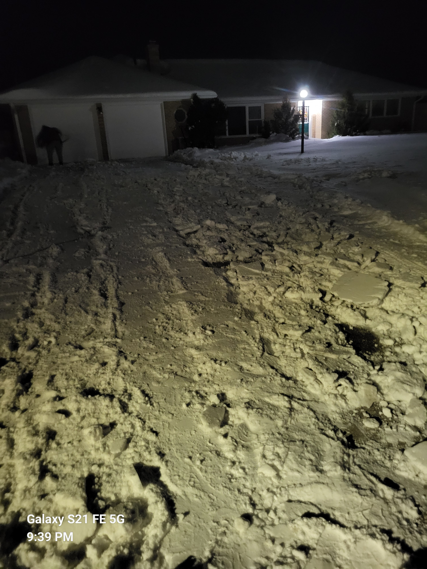 Driveway buried under deep, rutted snow at night before plowing